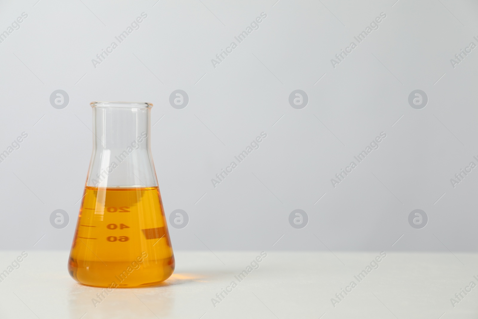 Photo of Glass flask with yellow oil on white table, space for text