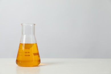 Photo of Glass flask with yellow oil on white table, space for text