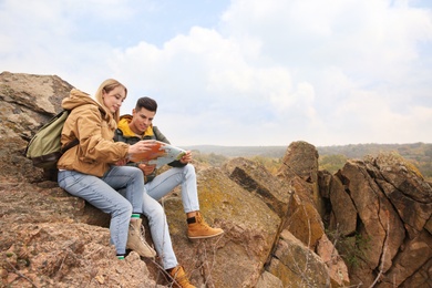 Couple of travelers with backpacks and map sitting on steep cliff. Autumn vacation