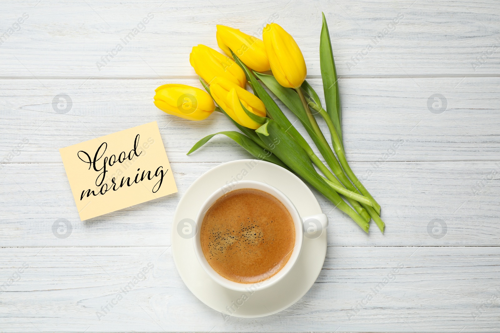 Image of Yellow tulips, coffee and card with text Good morning on white wooden table, flat lay  