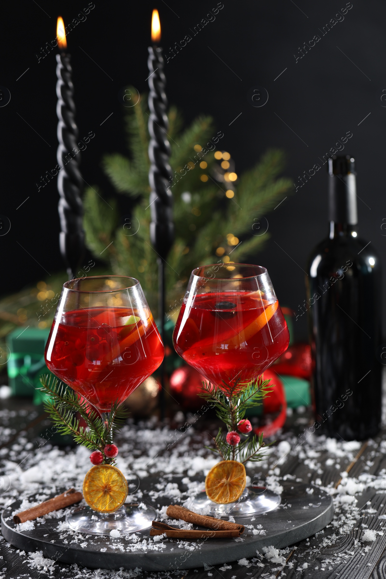 Photo of Christmas Sangria cocktail in glasses, burning candles and snow on dark wooden table