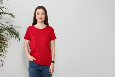 Photo of Young woman in t-shirt near light wall. Mock up for design