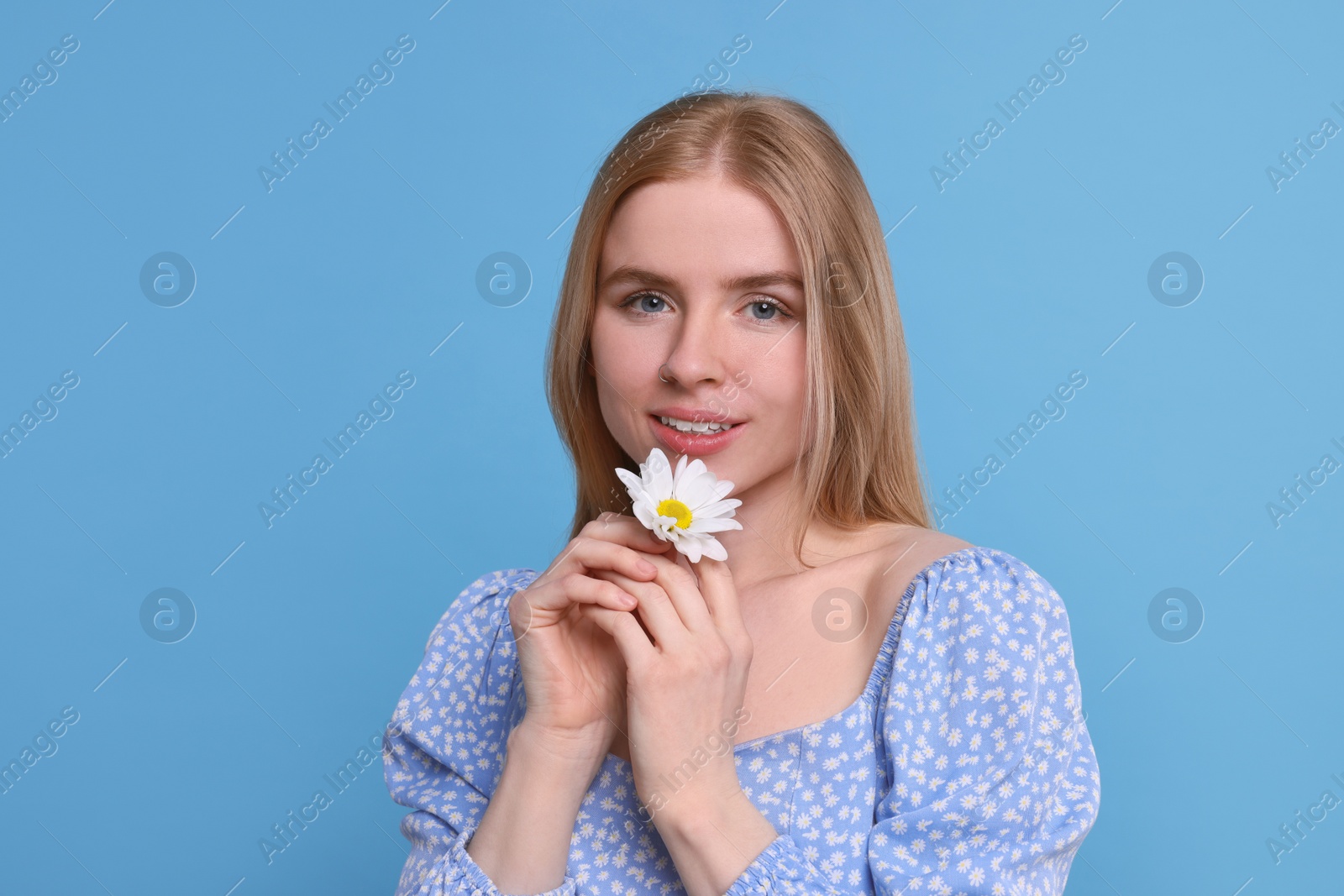 Photo of Beautiful woman with spring flower in hands on light blue background