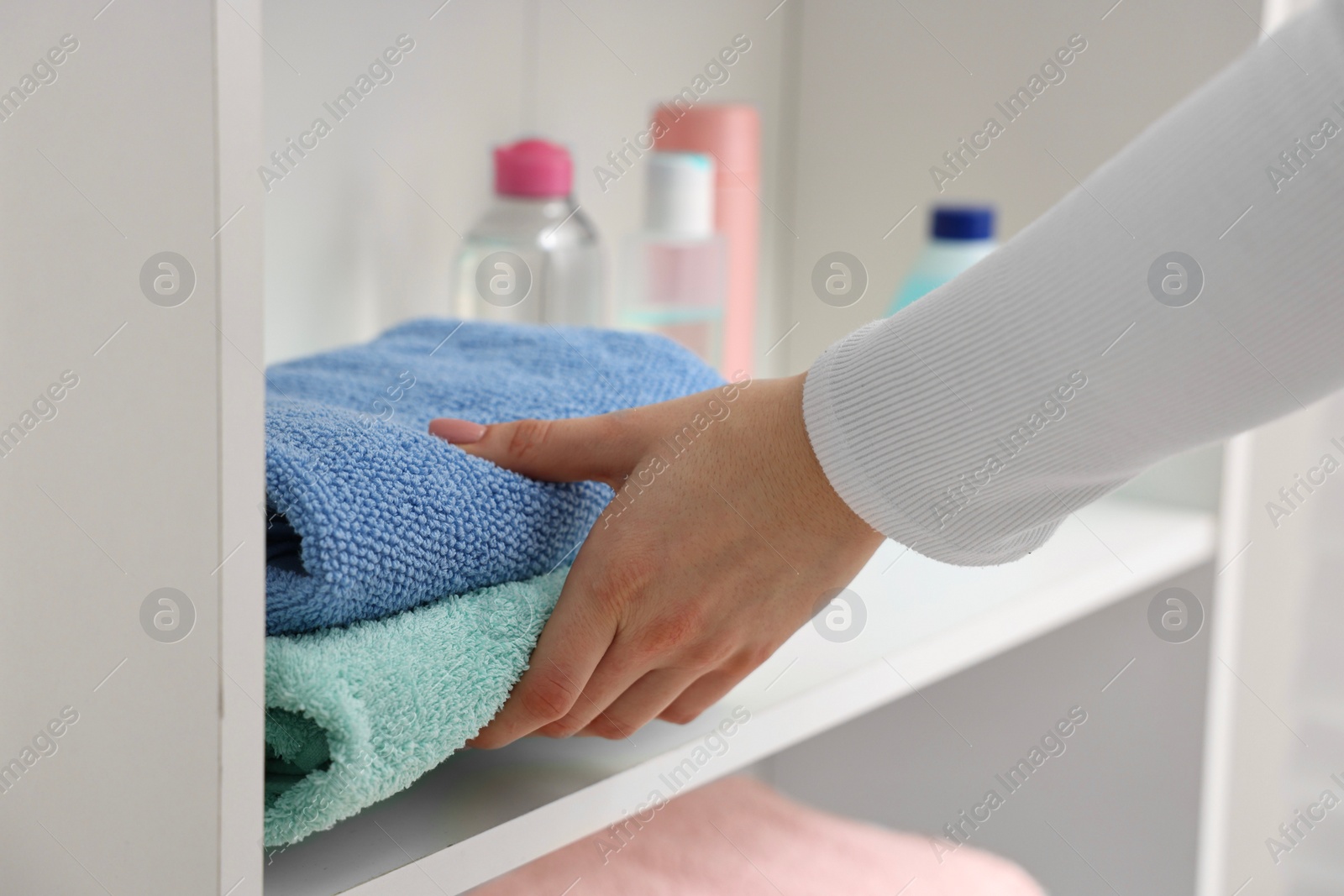 Photo of Woman stacking clean towels on shelf indoors, closeup