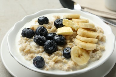 Photo of Tasty oatmeal with banana, blueberries, butter and milk served in bowl on light grey table, closeup
