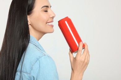 Beautiful happy woman drinking from red beverage can on light grey background