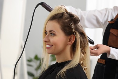 Hair styling. Hairdresser curling woman's hair in salon, closeup