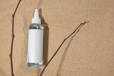 Photo of Bottle with serum and branches on sand, top view with space for text. Cosmetic product