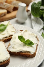 Photo of Bread with cream cheese and basil on plate, closeup