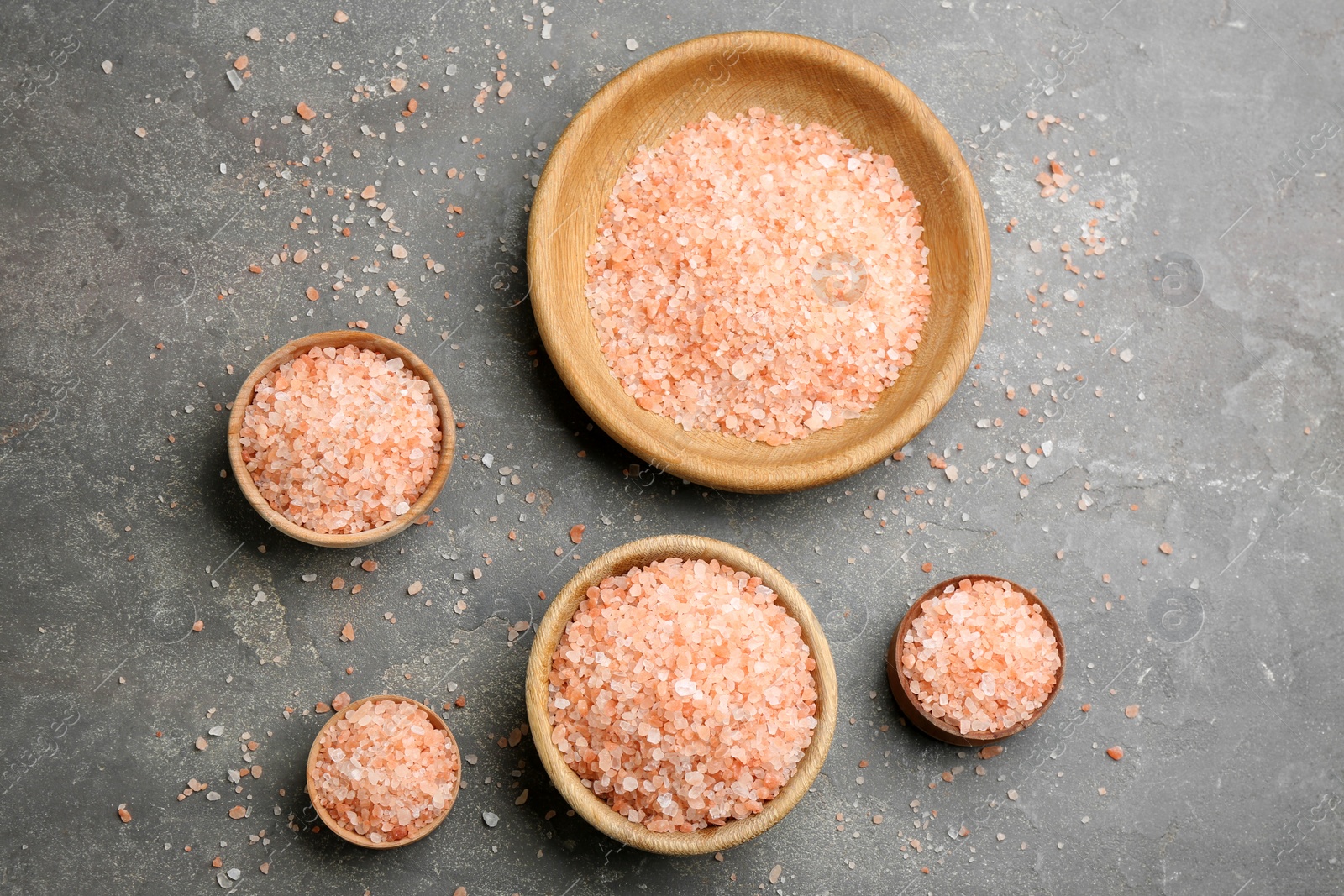 Photo of Pink himalayan salt in wooden bowls on grey table, flat lay