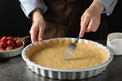 Photo of Shortcrust pastry. Woman making holes in raw dough with fork at grey table, closeup