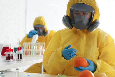 Scientist in chemical protective suit injecting orange at laboratory, space for text