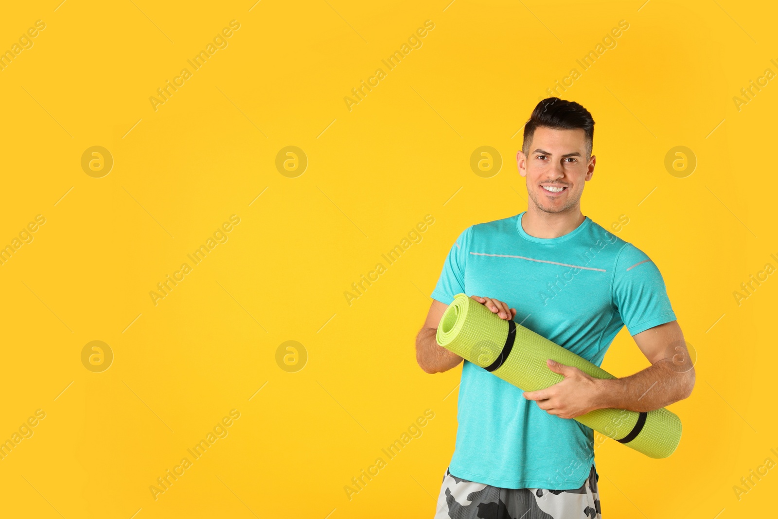 Photo of Handsome man with yoga mat on yellow background. Space for text