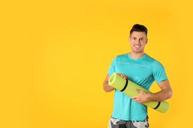 Photo of Handsome man with yoga mat on yellow background. Space for text