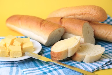 Photo of Cut baguette with fresh butter on yellow background, closeup