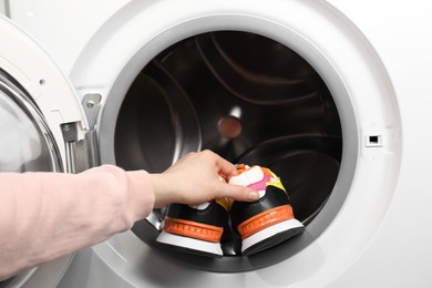 Photo of Woman putting stylish sneakers into washing machine, closeup