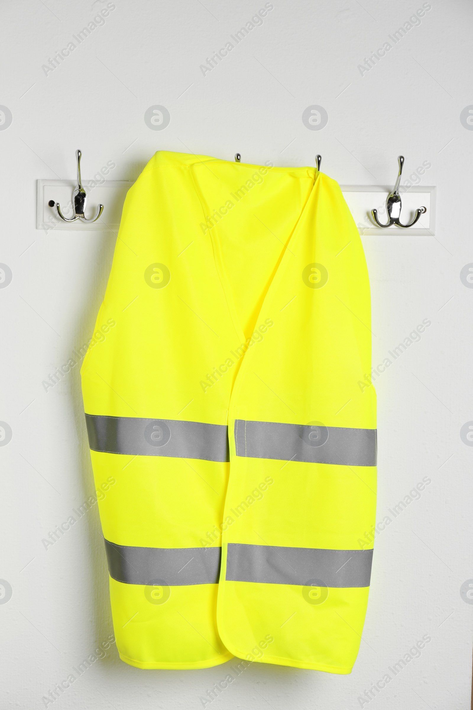 Photo of Reflective vest hanging on white wall. Safety equipment