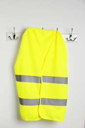 Photo of Reflective vest hanging on white wall. Safety equipment