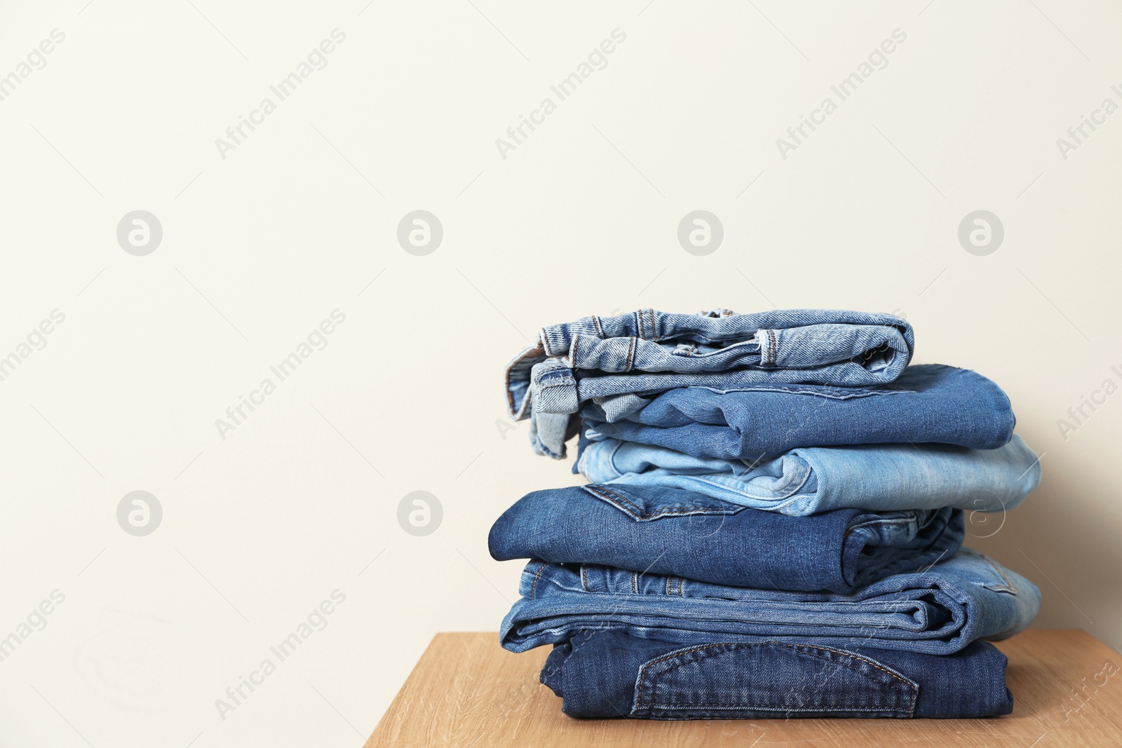 Photo of Stack of different jeans on table against light background. Space for text