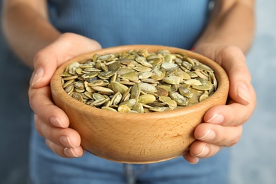 Photo of Young woman with bowl of raw pumpkin seeds on light blue background, closeup