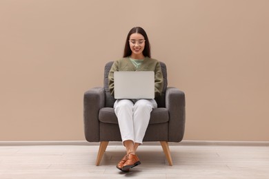 Photo of Beautiful woman with laptop sitting in armchair near beige wall indoors