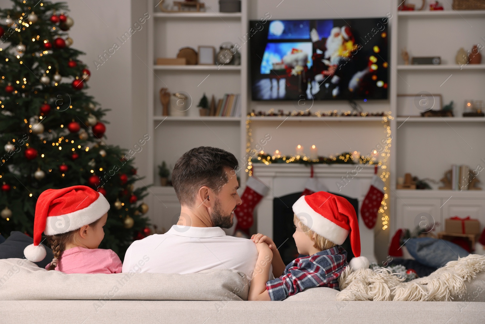 Photo of Happy father with his children spending time near TV in cosy room, back view. Christmas atmosphere