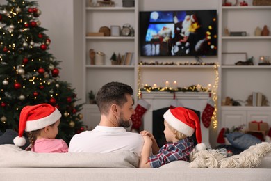 Happy father with his children spending time near TV in cosy room, back view. Christmas atmosphere