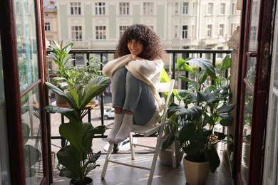 Photo of Beautiful young woman relaxing in chair surrounded by green houseplants on balcony