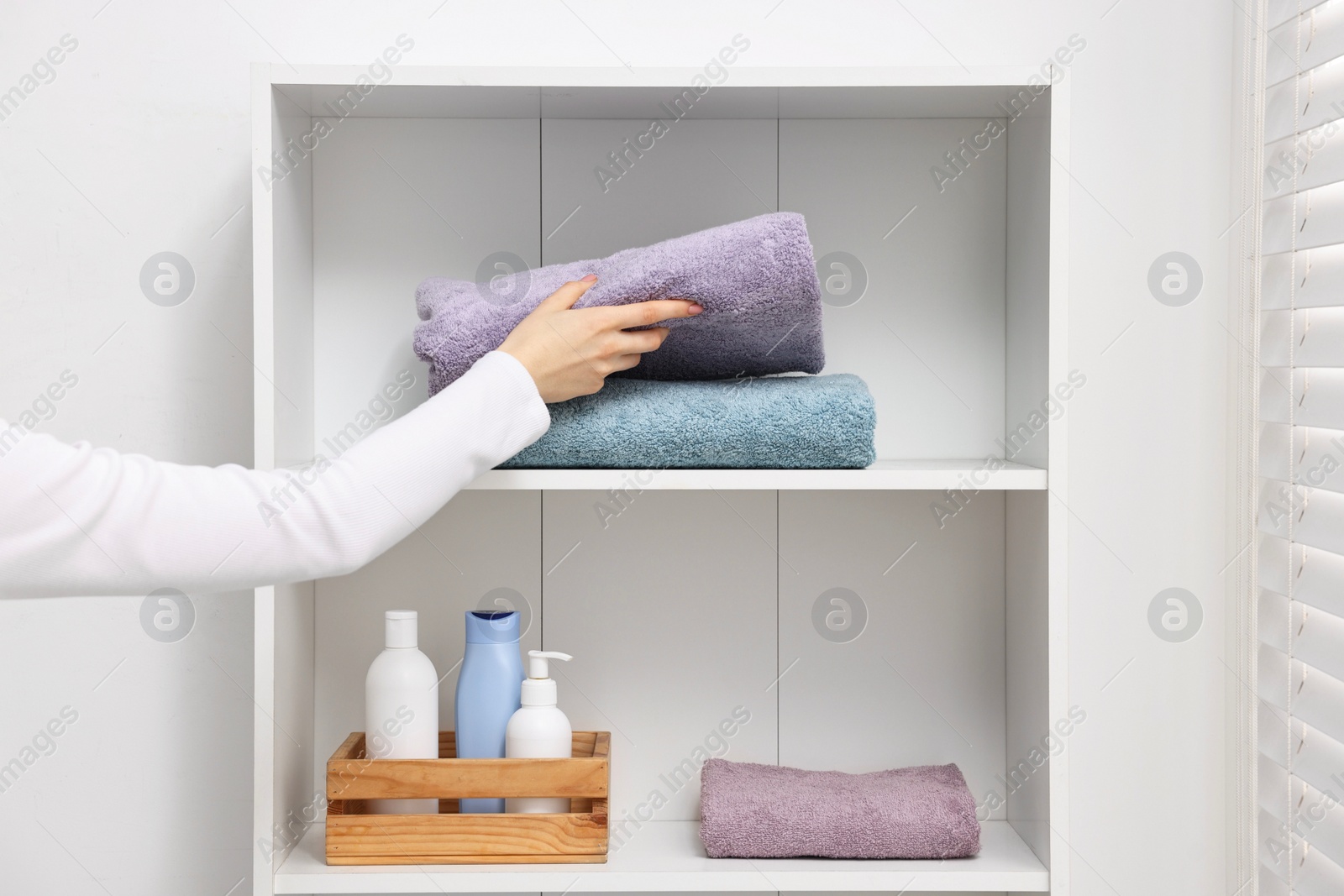 Photo of Woman stacking clean towels on shelf indoors, closeup