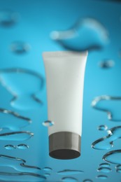 Moisturizing cream in tube on glass with water drops against blue background, low angle view