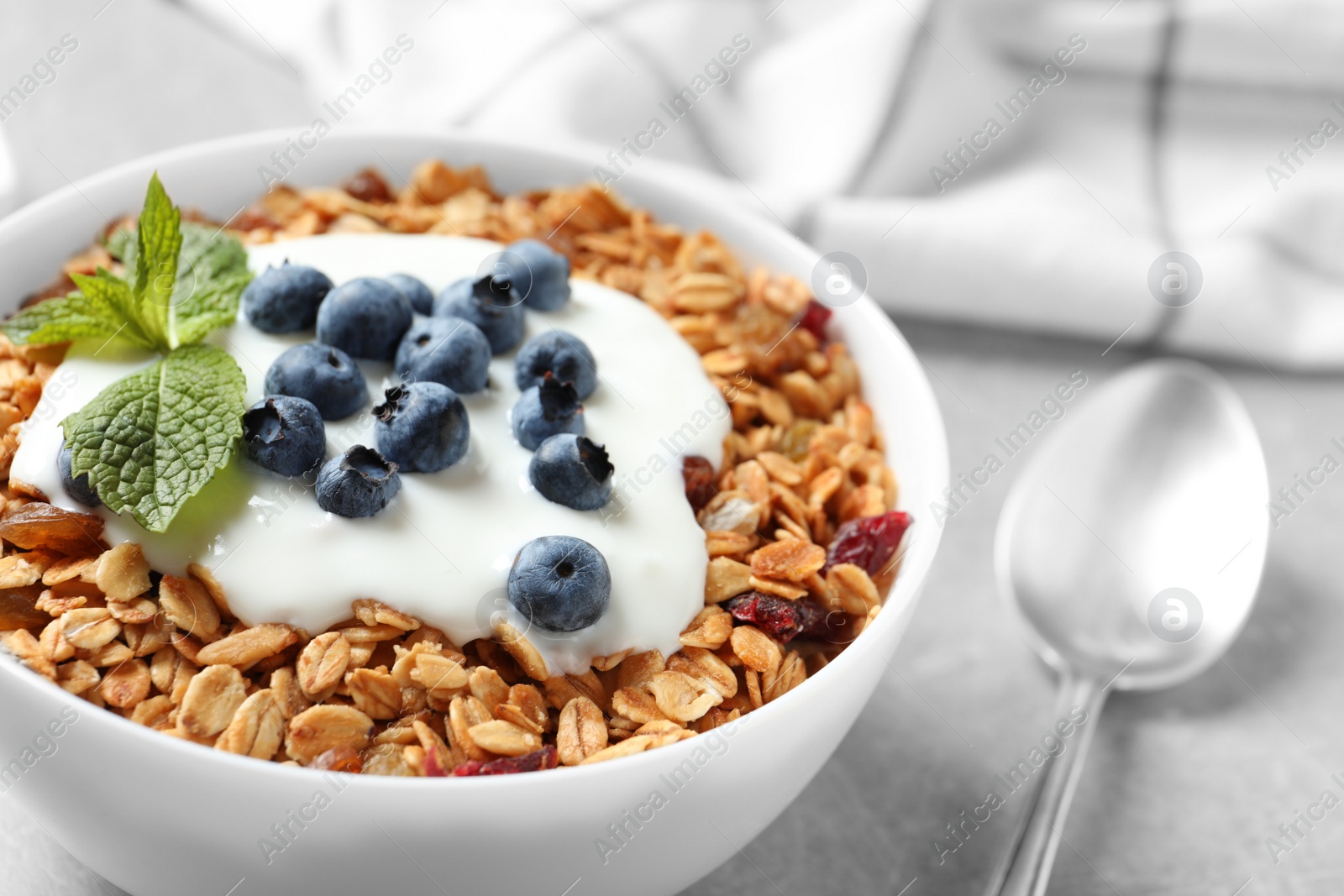 Photo of Delicious yogurt with granola and blueberries served on grey table, closeup