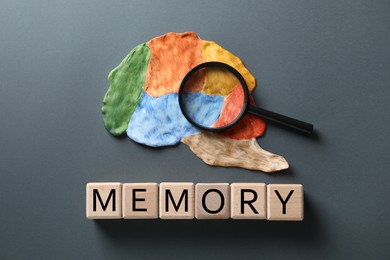 Photo of Word Amnesia made of wooden cubes, magnifying glass and brain with sections on grey background, flat lay