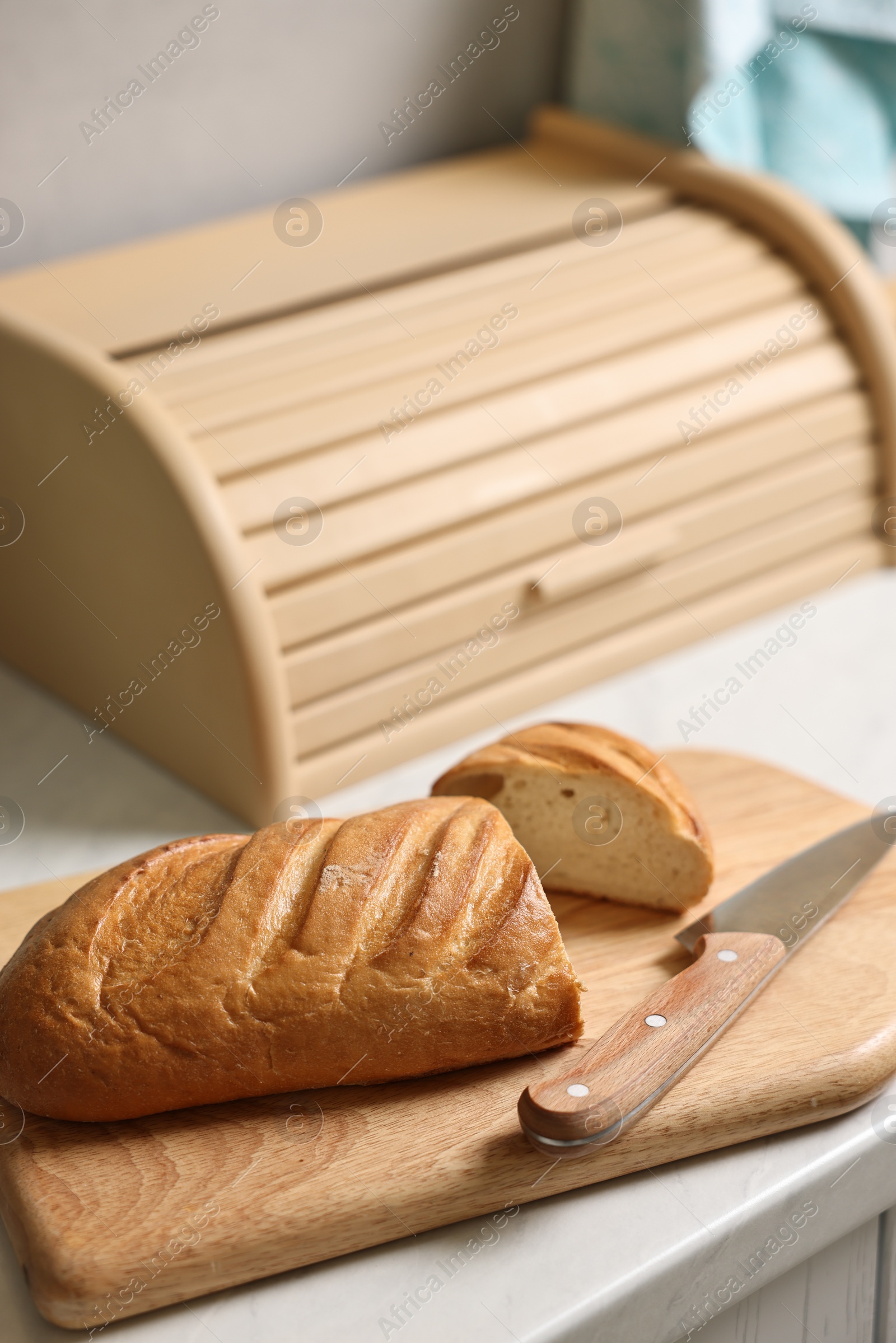 Photo of Wooden bread basket, freshly baked loaf on white marble table in kitchen