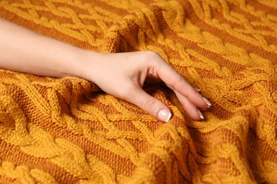 Photo of Woman touching soft orange knitted fabric, closeup view
