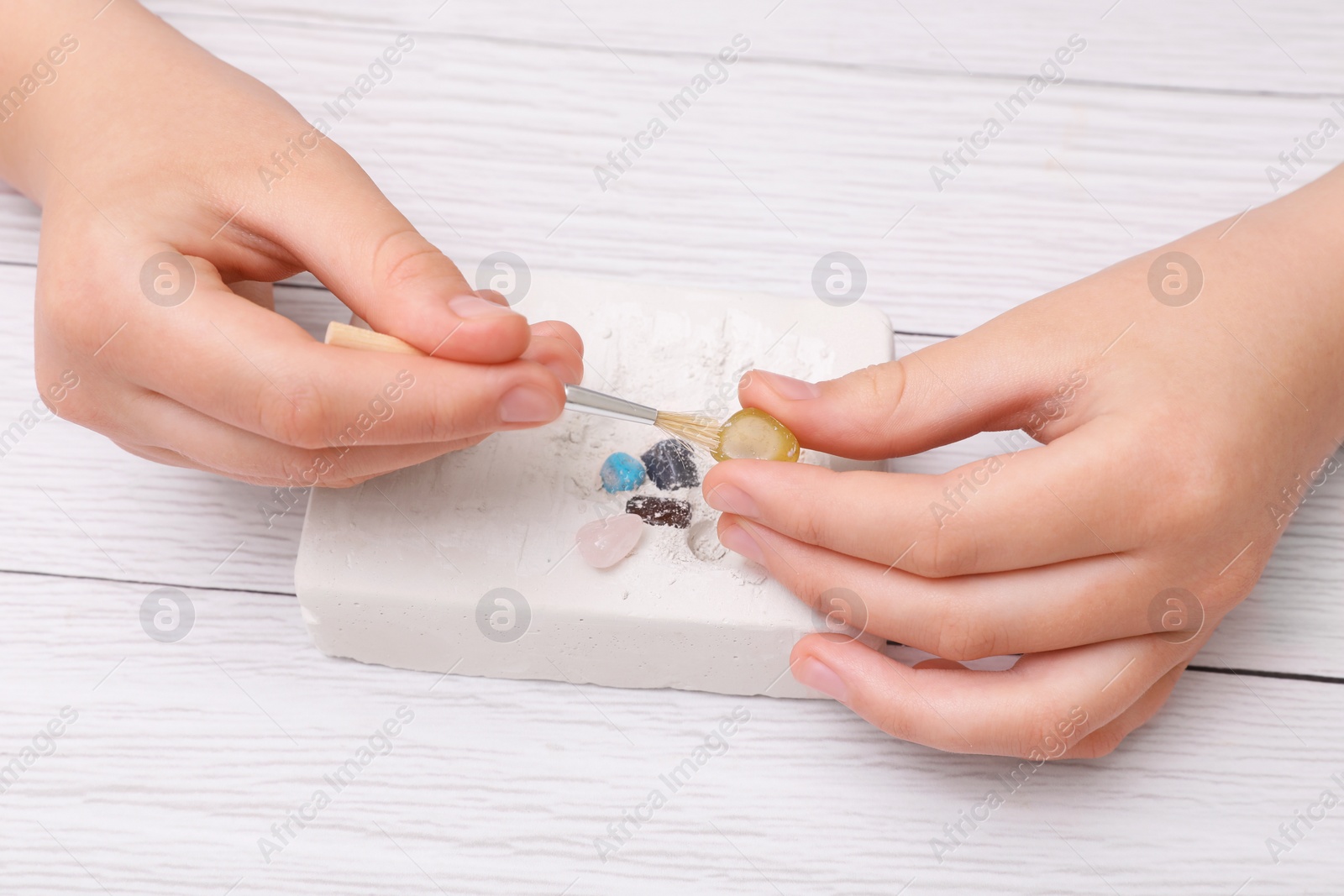 Photo of Child playing with Excavation kit at white wooden table, closeup. Educational toy for motor skills