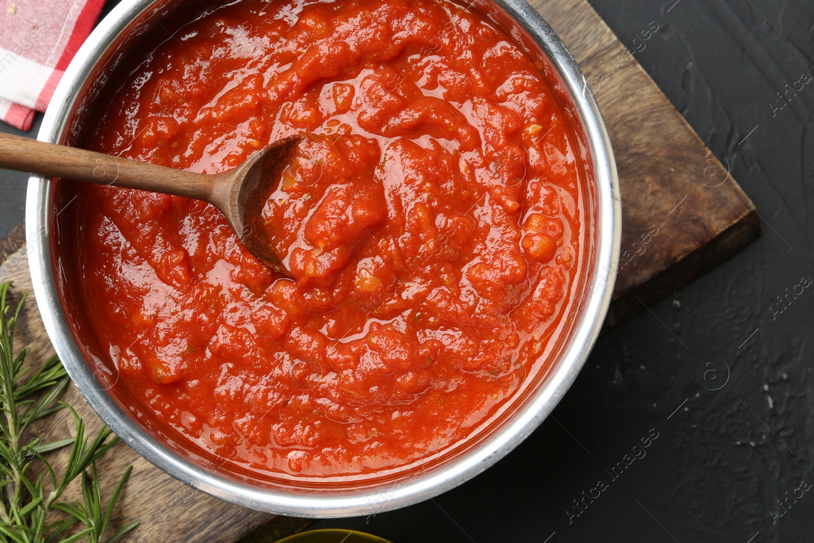 Photo of Homemade tomato sauce and spoon in pot on dark textured table, flat lay