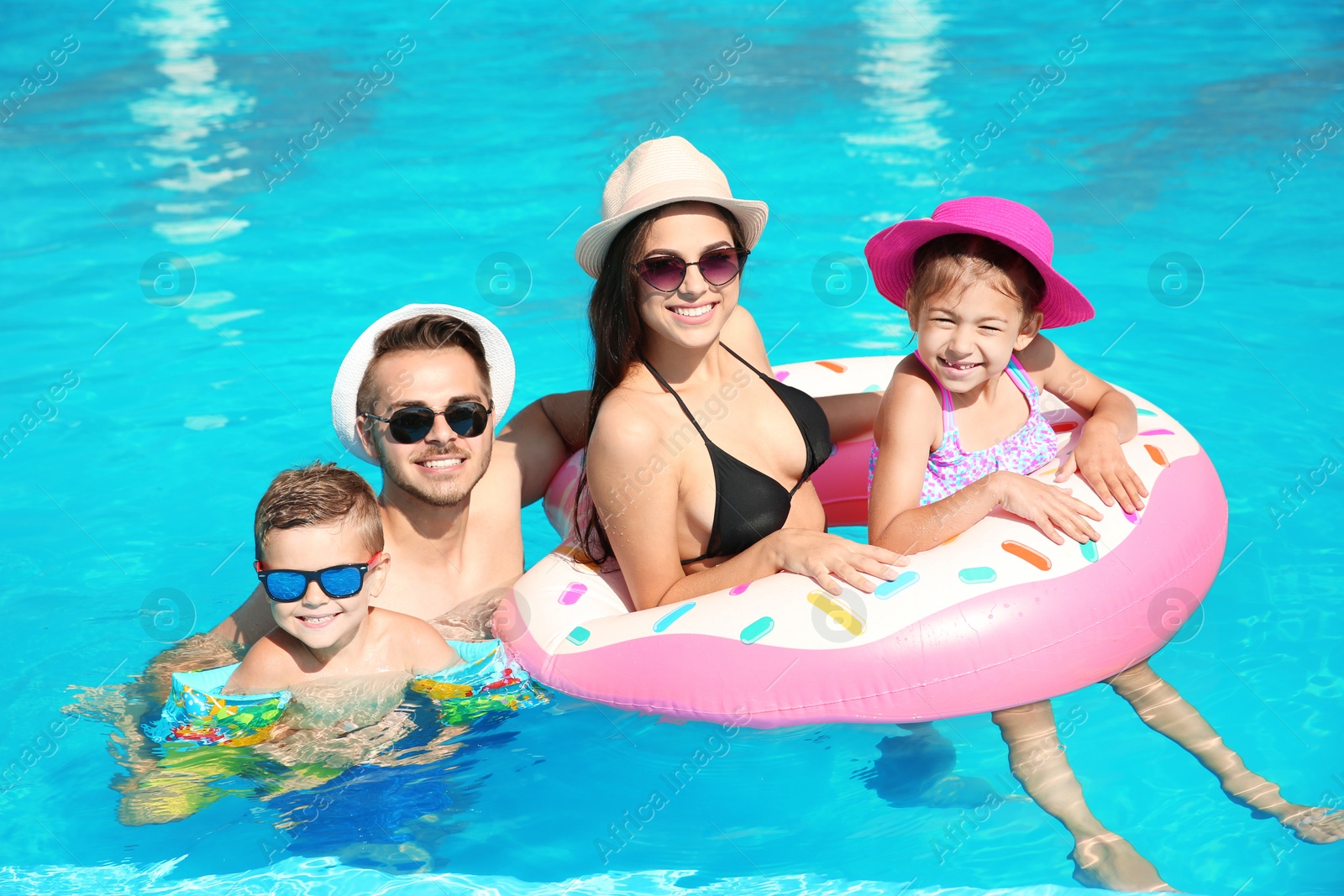 Photo of Young family with little children in swimming pool on sunny day