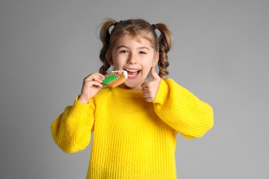 Cute little girl with Christmas gingerbread cookie on light grey background