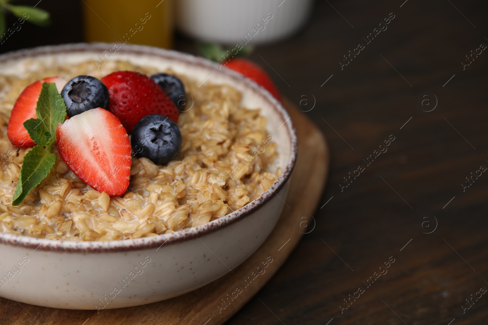 Photo of Tasty oatmeal with strawberries and blueberries in bowl on wooden table, closeup. Space for text