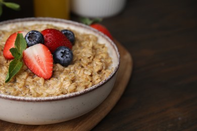 Photo of Tasty oatmeal with strawberries and blueberries in bowl on wooden table, closeup. Space for text