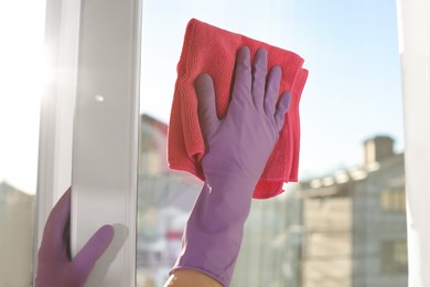 Photo of Young woman cleaning window glass with rag at home, closeup