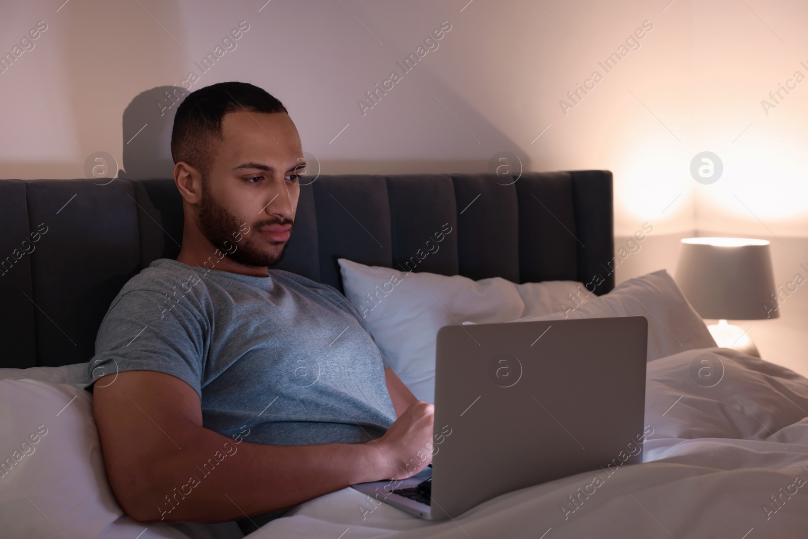 Photo of Young man using laptop in bed at night. Internet addiction