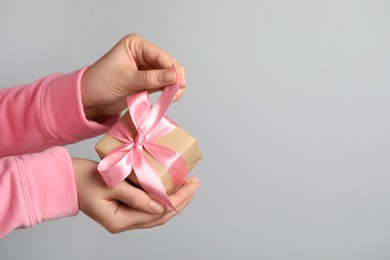 Photo of Woman holding gift box with pink bow on light grey background, closeup. Space for text