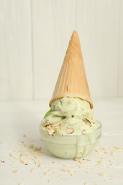 Delicious pistachio ice cream with chopped nuts in wafer cone on white wooden table