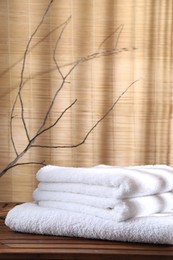 Photo of Stacked soft towels on wooden table and tree branches indoors