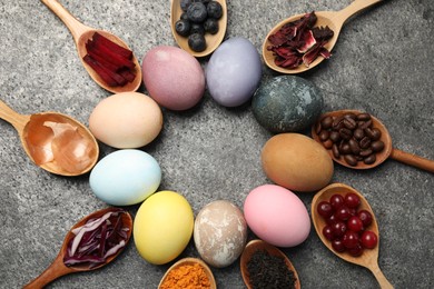 Naturally painted Easter eggs on grey table, flat lay. Turmeric, cranberries, red cabbage, onion, beetroot, blueberries, hibiscus, coffee beans and tea used for coloring
