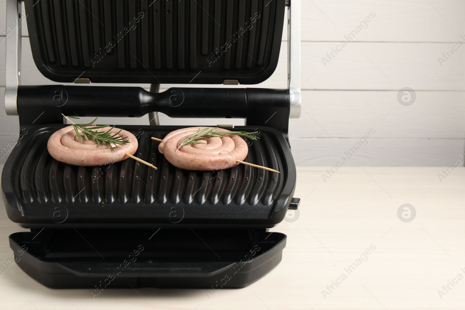 Photo of Electric grill with homemade sausages and rosemary on wooden table. Space for text