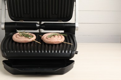 Photo of Electric grill with homemade sausages and rosemary on wooden table. Space for text