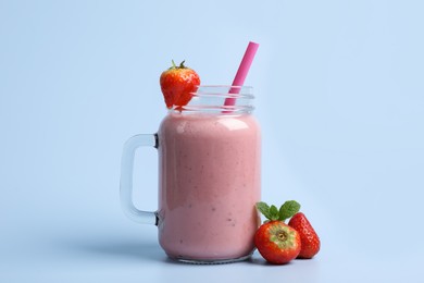 Photo of Mason jar with delicious berry smoothie and fresh strawberries on light blue background