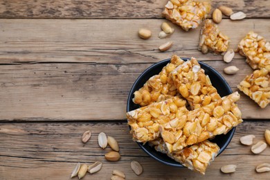 Photo of Delicious peanut kozinaki bars in bowl on wooden table, flat lay. Space for text